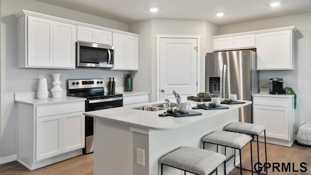 kitchen featuring sink, light hardwood / wood-style flooring, appliances with stainless steel finishes, white cabinetry, and an island with sink