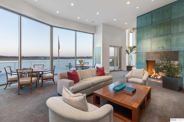 carpeted living room with a water view, a towering ceiling, plenty of natural light, and a fireplace