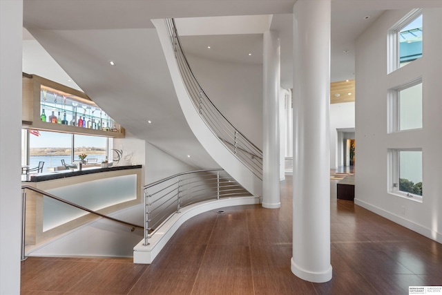 stairway featuring wood-type flooring, ornate columns, a high ceiling, and a water view