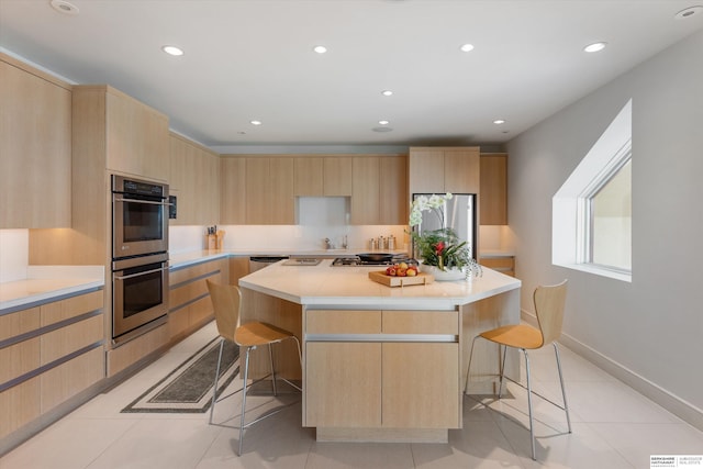 kitchen featuring a kitchen island, appliances with stainless steel finishes, light brown cabinets, and a kitchen bar