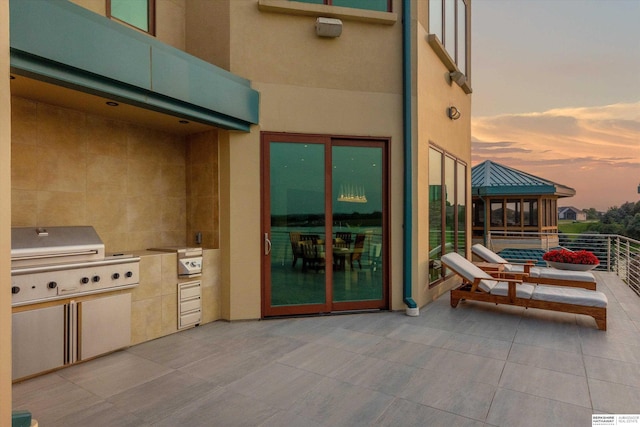 patio terrace at dusk featuring exterior kitchen, a balcony, and grilling area