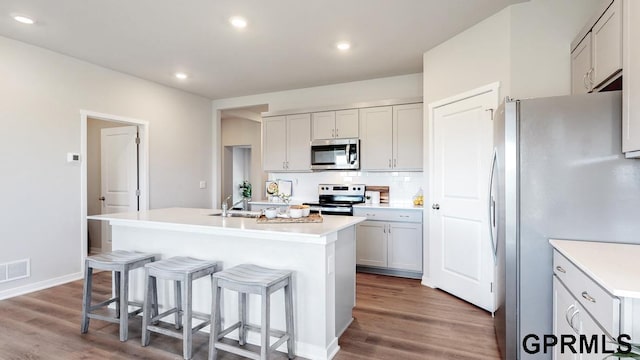 kitchen featuring a breakfast bar, an island with sink, stainless steel appliances, hardwood / wood-style floors, and backsplash