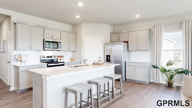 kitchen featuring sink, appliances with stainless steel finishes, a center island with sink, a kitchen bar, and decorative backsplash