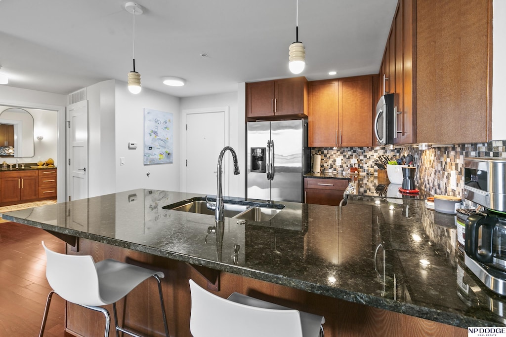 kitchen featuring pendant lighting, sink, a breakfast bar, backsplash, and stainless steel appliances