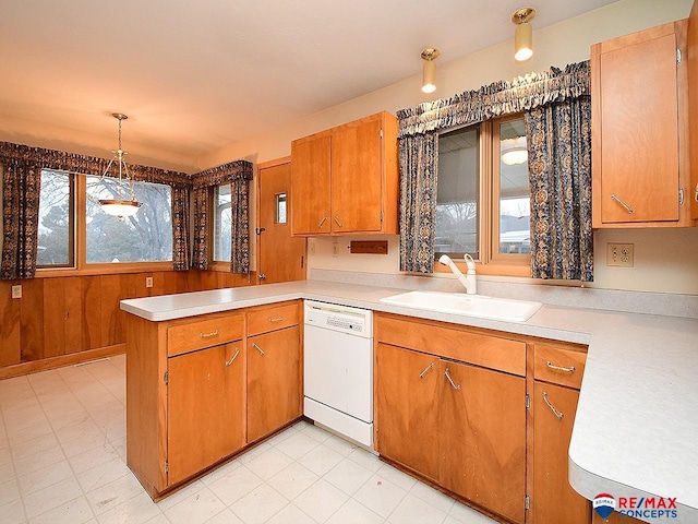 kitchen with wood walls, sink, hanging light fixtures, white dishwasher, and kitchen peninsula