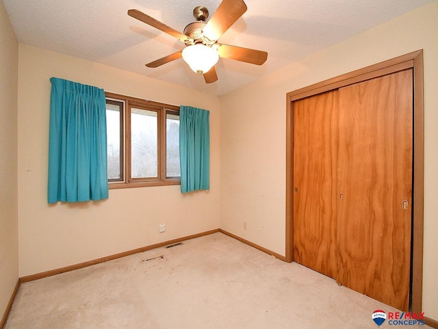 unfurnished bedroom featuring light carpet, ceiling fan, a closet, and a textured ceiling