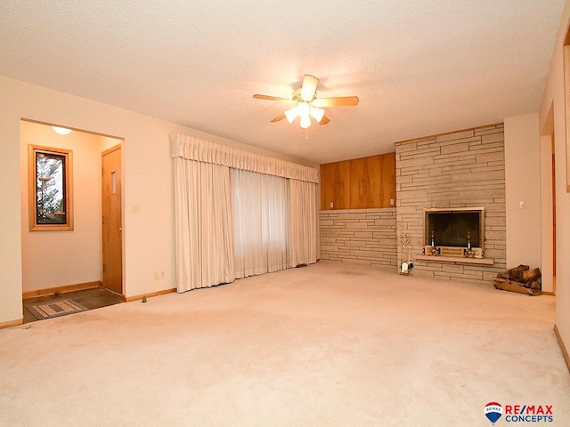 unfurnished living room featuring ceiling fan, a stone fireplace, light colored carpet, and a textured ceiling