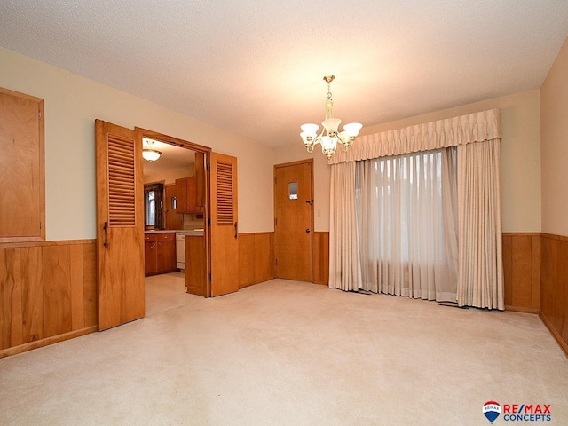 carpeted empty room with a textured ceiling, a chandelier, and wood walls