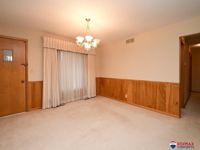 carpeted spare room with a chandelier, a textured ceiling, and wood walls