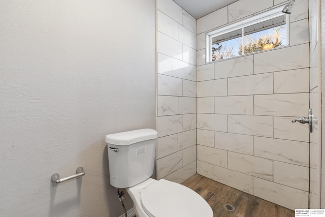 bathroom with hardwood / wood-style floors, toilet, and tiled shower