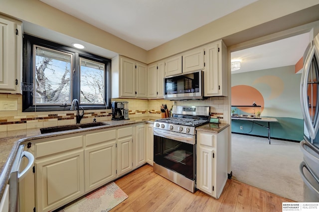 kitchen with stainless steel appliances, sink, light wood-type flooring, and decorative backsplash