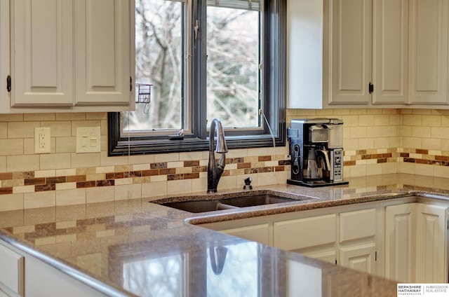 kitchen with light stone countertops, sink, decorative backsplash, and white cabinets