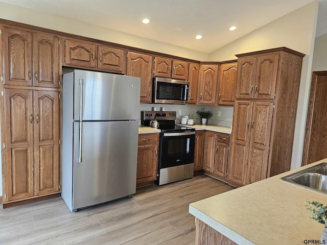 kitchen featuring lofted ceiling, sink, light wood-type flooring, and appliances with stainless steel finishes