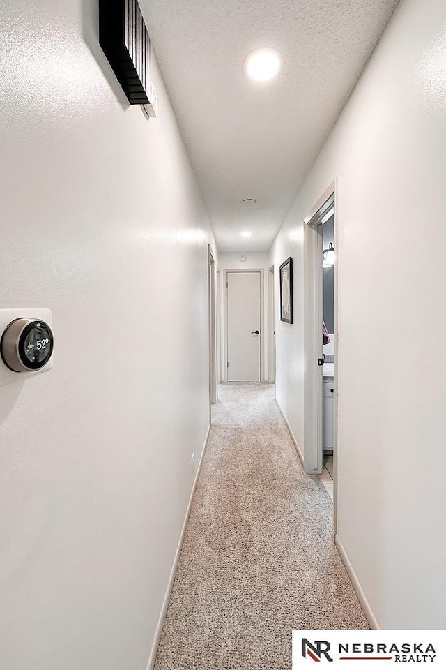 corridor featuring light colored carpet and a textured ceiling