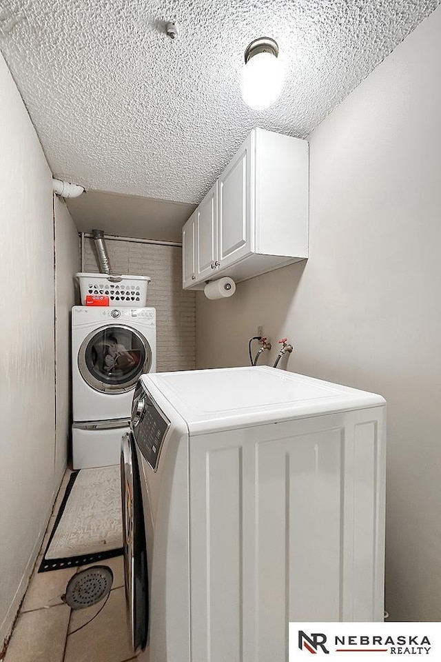 washroom with cabinets, washing machine and clothes dryer, tile patterned floors, and a textured ceiling