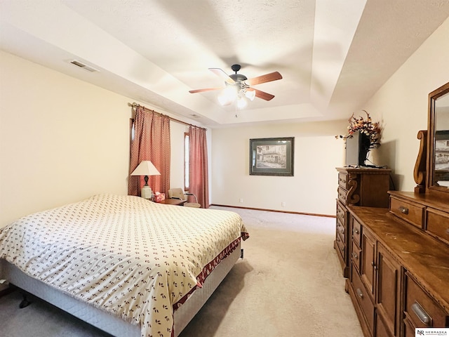 carpeted bedroom featuring a textured ceiling, ceiling fan, and a tray ceiling