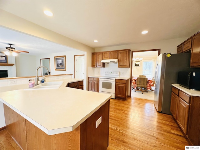 kitchen featuring sink, white range with electric cooktop, decorative backsplash, a large island with sink, and light wood-type flooring