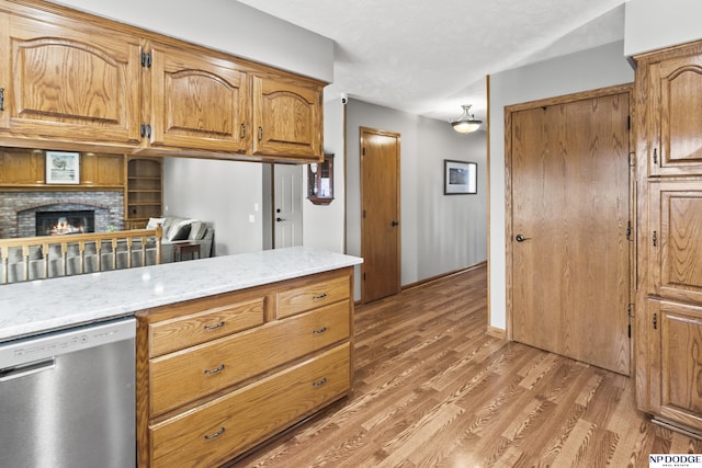 kitchen with light stone counters, stainless steel dishwasher, wood-type flooring, and a brick fireplace