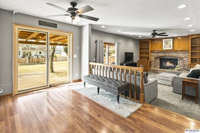 living room featuring ceiling fan, a textured ceiling, a fireplace, and light hardwood / wood-style flooring