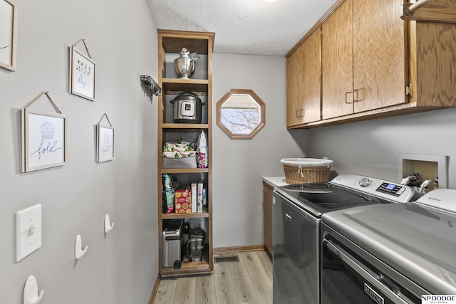 laundry room with cabinets, light wood-type flooring, a textured ceiling, and washer and clothes dryer