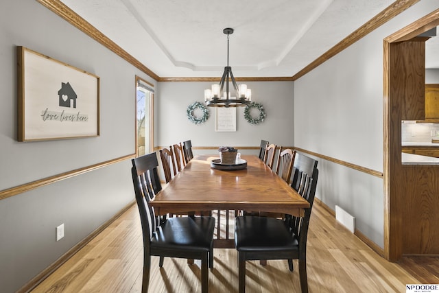 dining space with crown molding, an inviting chandelier, light wood-type flooring, and a tray ceiling