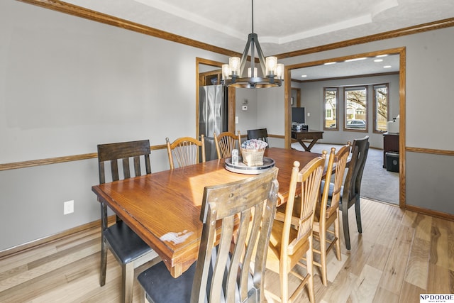 dining space with a notable chandelier, crown molding, light hardwood / wood-style floors, and a raised ceiling