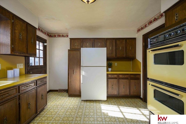 kitchen featuring white refrigerator, multiple ovens, and dark brown cabinets