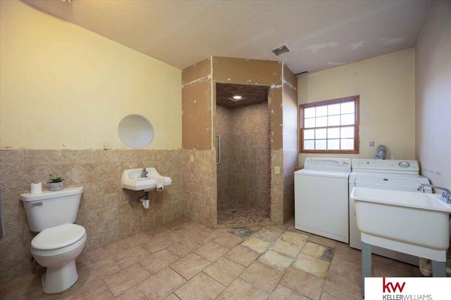 bathroom with sink, tile walls, separate washer and dryer, a shower with shower door, and toilet