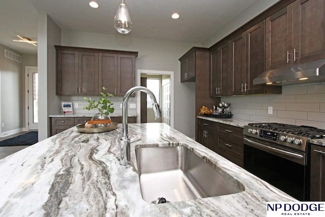 kitchen featuring sink, stainless steel gas stove, light stone counters, tasteful backsplash, and dark brown cabinetry