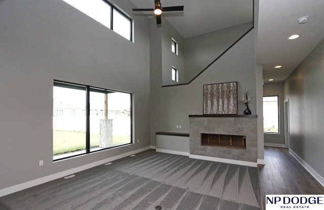 unfurnished living room with a tile fireplace, a towering ceiling, ceiling fan, and dark hardwood / wood-style flooring