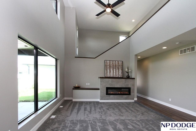 unfurnished living room featuring ceiling fan, a towering ceiling, a fireplace, and dark hardwood / wood-style flooring