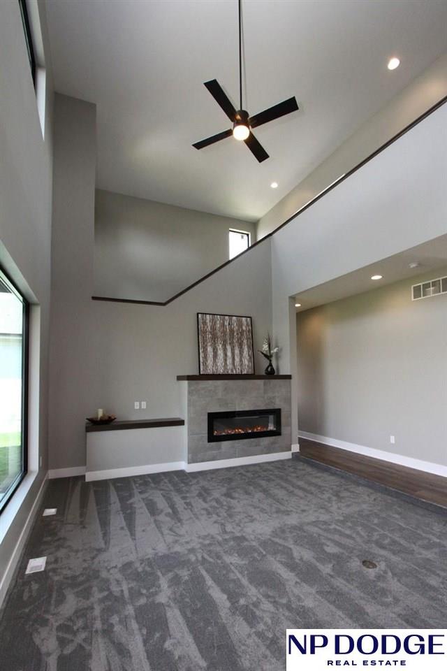 unfurnished living room with dark colored carpet, a tile fireplace, a towering ceiling, and ceiling fan