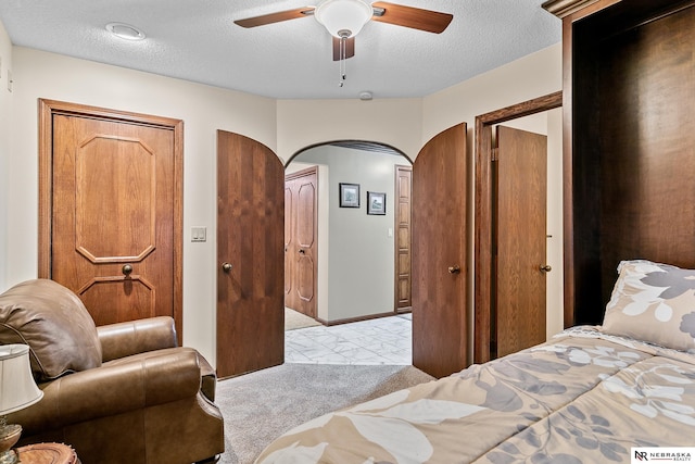 bedroom with light carpet, ceiling fan, two closets, and a textured ceiling