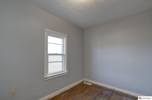 empty room featuring a textured ceiling, dark wood-style flooring, visible vents, and baseboards