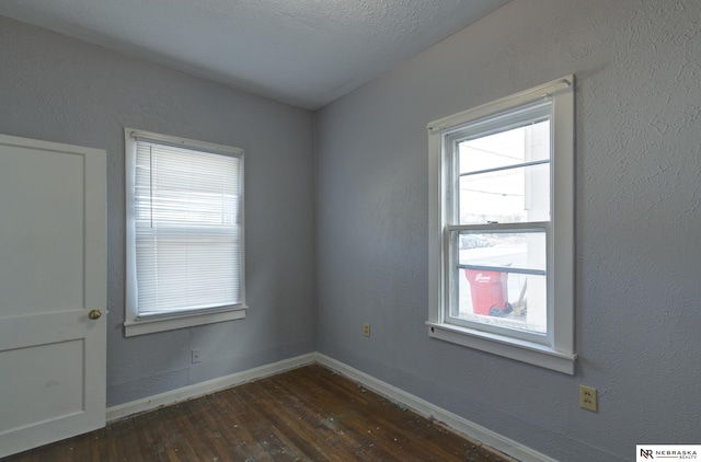 spare room with baseboards, dark wood finished floors, and a textured wall