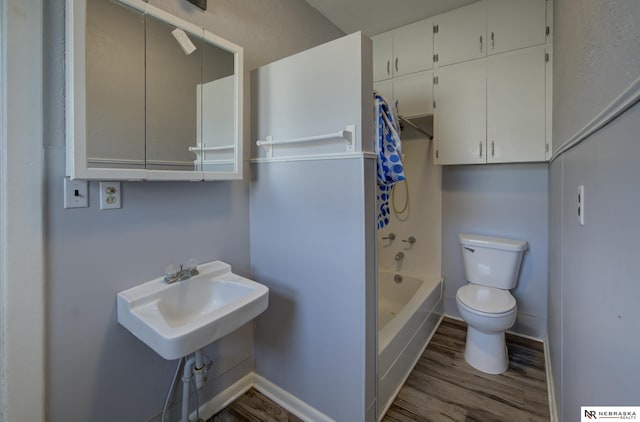 bathroom with shower / bathtub combination, toilet, a sink, wood finished floors, and baseboards