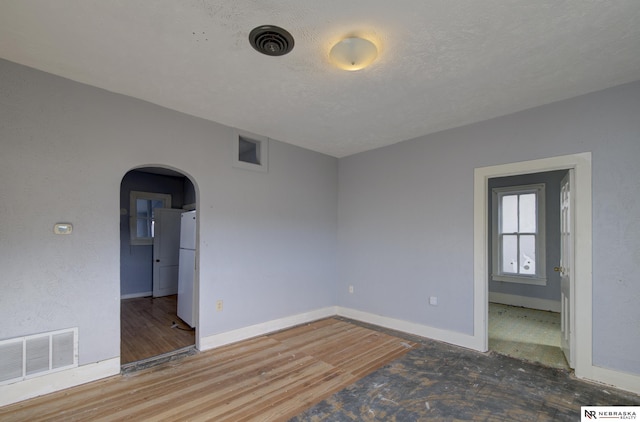 empty room with arched walkways, visible vents, a textured ceiling, and wood finished floors