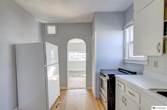 kitchen with arched walkways, electric stove, freestanding refrigerator, light wood-style floors, and white cabinetry