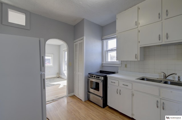 kitchen with arched walkways, light wood-style flooring, a sink, freestanding refrigerator, and stainless steel electric range oven