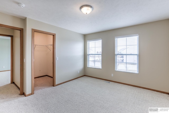 unfurnished bedroom with light carpet, a walk in closet, a closet, and a textured ceiling