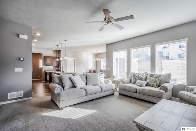 carpeted living room with sink, ceiling fan with notable chandelier, and a textured ceiling