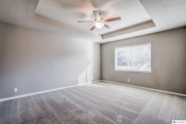 carpeted empty room featuring a raised ceiling, ceiling fan, and a textured ceiling