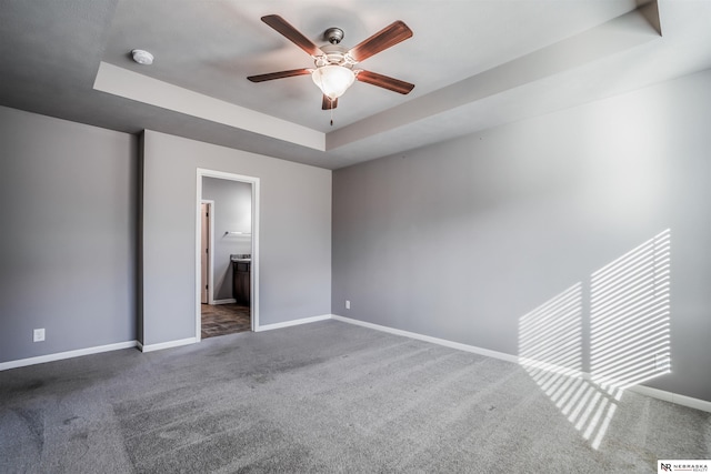 unfurnished bedroom featuring ceiling fan, connected bathroom, a raised ceiling, and dark carpet