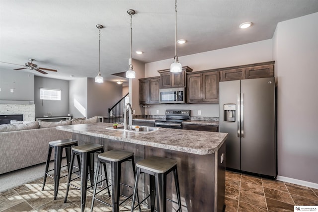 kitchen with sink, appliances with stainless steel finishes, dark brown cabinetry, a center island with sink, and decorative light fixtures