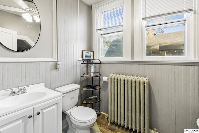 bathroom featuring toilet, radiator heating unit, wooden walls, vanity, and hardwood / wood-style flooring