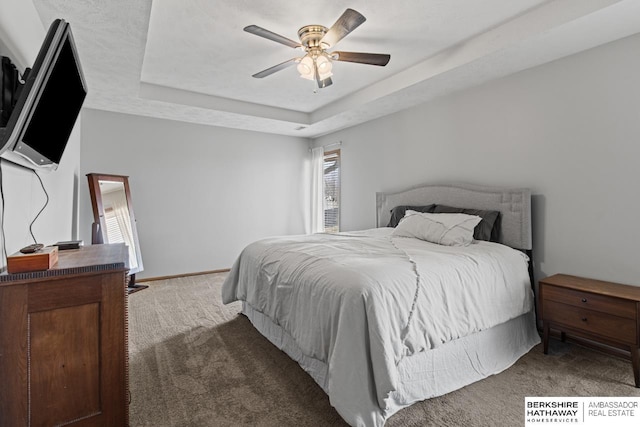 carpeted bedroom with a raised ceiling and ceiling fan