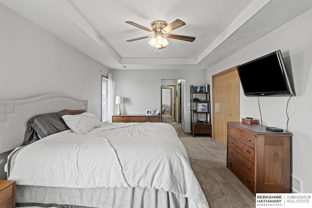 bedroom featuring a tray ceiling, light colored carpet, and ceiling fan