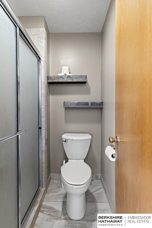 bathroom with toilet, a textured ceiling, and a shower with shower door