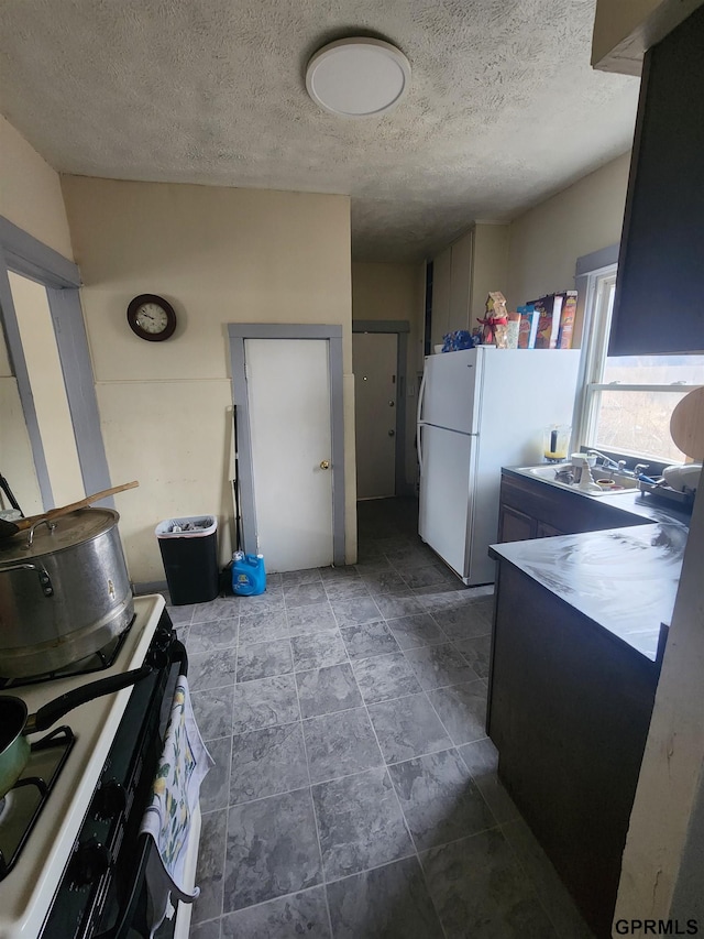 kitchen with sink, gas range oven, a textured ceiling, and white refrigerator