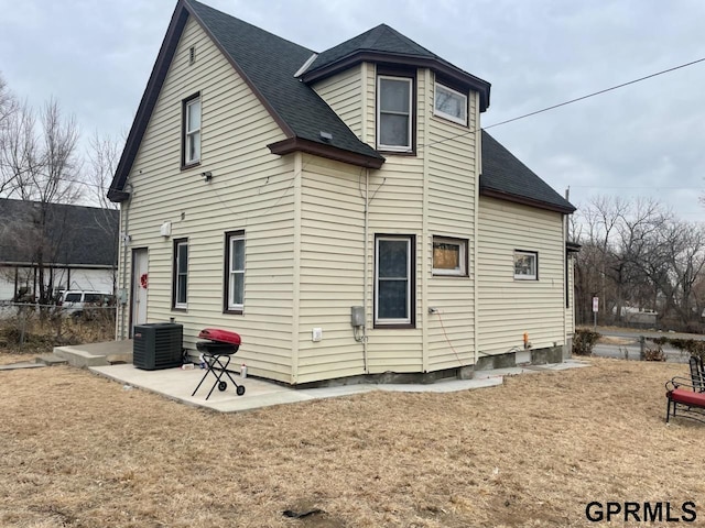 rear view of house with cooling unit, a patio area, and a lawn